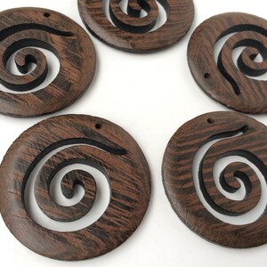 Pode incluir: Seis ornamentos redondos de madeira castanho com um desenho de espiral preto. Cada ornamento tem um furo na parte superior para pendurar.