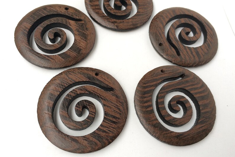 Pode incluir: Seis ornamentos redondos de madeira castanho com um desenho de espiral preto. Cada ornamento tem um furo na parte superior para pendurar.