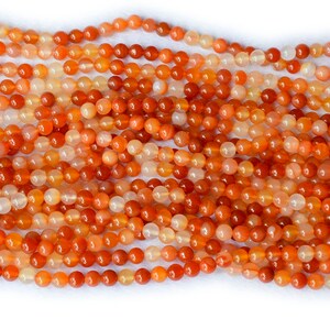 May include: A strand of orange carnelian beads. The beads are round and smooth, with a natural, polished finish.