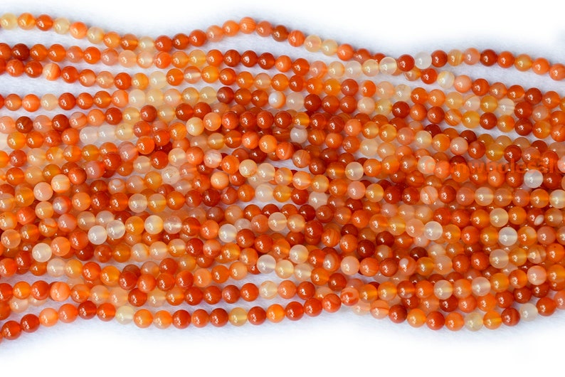May include: A strand of orange carnelian beads. The beads are round and smooth, with a natural, polished finish.