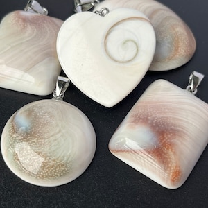 May include: Five shell pendants with silver bail attachments. The pendants are in the shapes of a heart, a circle, and two rectangles. The shells are a light cream colour with brown and white swirls and patterns.