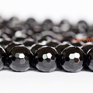 May include: Close-up of a strand of faceted black onyx beads. The beads are round with a multi-faceted surface, reflecting light. The beads are strung together, creating a dark, textured pattern. The background is white.