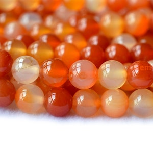 May include: A strand of round, orange carnelian beads. The beads are smooth and polished, with a translucent quality.