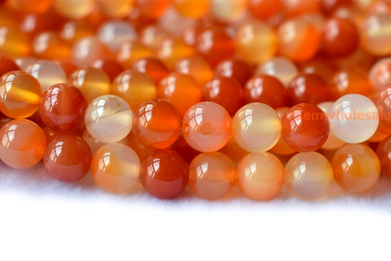 May include: A strand of round, orange carnelian beads. The beads are smooth and polished, with a translucent quality.