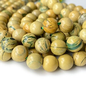 May include: A strand of round, light green and brown patterned beads. The beads are made of natural stone and have a smooth, polished finish.
