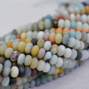 Pode incluir: Primeiro plano de fios de contas de pedra preciosa Amazonita. As contas são pequenas, planas e redondas, em tons de azul claro, amarelo e castanho. Têm um acabamento mate e são enfiadas, criando um efeito texturizado.