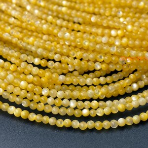May include: Close-up of strands of small, round, yellow beads. The beads have a slight sheen and are arranged in a layered pattern. The beads are a warm yellow colour, with some lighter, almost white, beads mixed in.