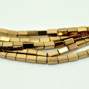 Peut inclure: Gros plan sur des brins de perles rectangulaires de couleur or. Les perles sont de taille et de forme uniformes, avec un éclat métallique. Les perles sont enfilées ensemble, créant un motif linéaire et fluide. Le texte "GemWholesale" est visible.