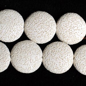 May include: Close-up of a strand of white, round beads with a textured, porous surface. The beads are arranged in two rows against a black background. The beads appear to be made of a natural material.
