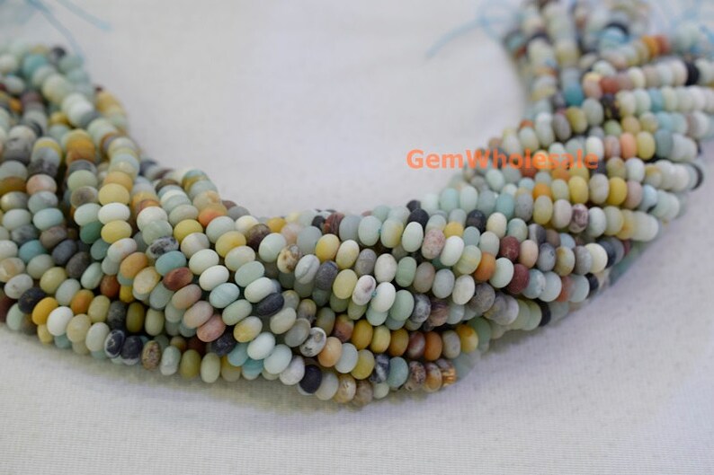 May include: Strands of Amazonite gemstone beads in a variety of colors, including shades of blue, green, yellow, and brown. The beads are small, round, and have a smooth texture. The beads are strung together, creating a necklace or bracelet.