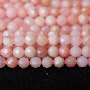 May include: A strand of pink opal beads with a faceted finish. The beads are round and have a smooth, polished surface.