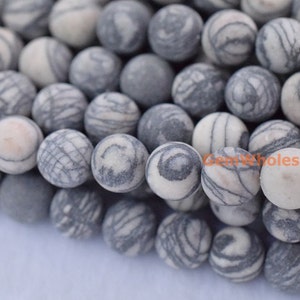 Puede incluir: Primer plano de una hebra de cuentas redondas, blancas y grises con patrones. Las cuentas tienen una textura natural ligeramente rugosa.