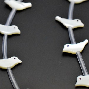 May include: A white pearl necklace with a string of white bird charms. Each bird charm has a small black eye.