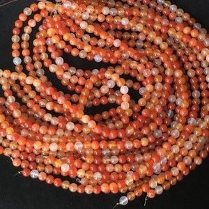 May include: A strand of orange carnelian beads. The beads are round and have a smooth, polished finish. They are strung on a clear thread.