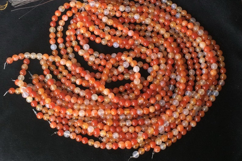 May include: A strand of orange carnelian beads. The beads are round and have a smooth, polished finish. They are strung on a clear thread.