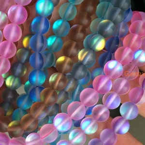May include: A strand of iridescent glass beads in shades of pink, blue, and brown. The beads are round and have a frosted finish.