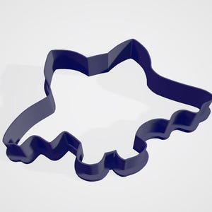 May include: A dark blue cookie cutter shaped like a bow. The cutter features a scalloped lower edge and a pointed top. The object is made of a solid material and is set against a white background.