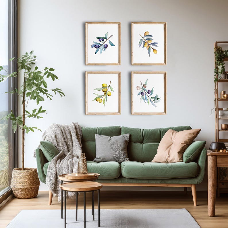 Op de afbeelding: Vier ingelijste aquarelprints van olijftakken met groene bladeren en zwarte of gele olijven hangen boven een groene fluwelen bank. De prints zitten in lichtbruine houten frames. Een potplant en een bijzettafel staan op de voorgrond.