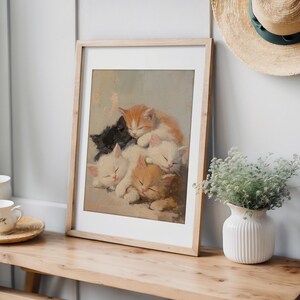May include: A framed painting of five kittens sleeping on top of each other. The kittens are white, orange, and black. The painting is in a light wood frame.