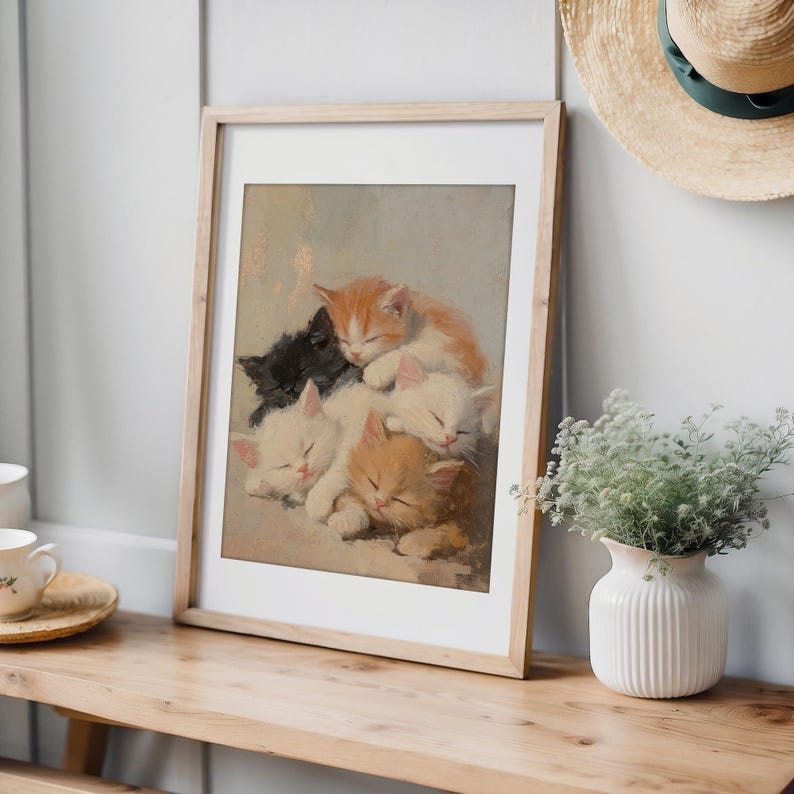 May include: A framed painting of five kittens sleeping on top of each other. The kittens are white, orange, and black. The painting is in a light wood frame.