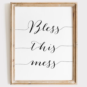 May include: A framed print with the text "Bless this mess" in black cursive script on a white background.
