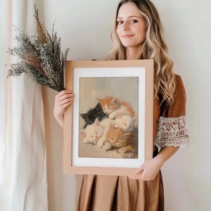 May include: A framed print of a painting depicting five kittens sleeping on top of each other. The kittens are white, orange, and black. The painting is set against a light brown background.