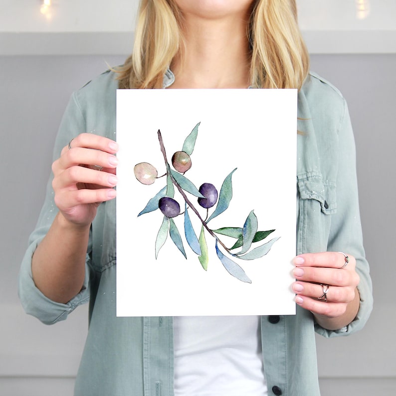 Op de afbeelding: Waterverfillustratie van een olijftak met groene bladeren en paarse olijven. Het kunstwerk heeft een delicaat, botanisch ontwerp met zachte aquareltexturen en een natuurlijke esthetiek. De olijven zijn dieppaars en de bladeren zijn een mix van groen en blauw.
