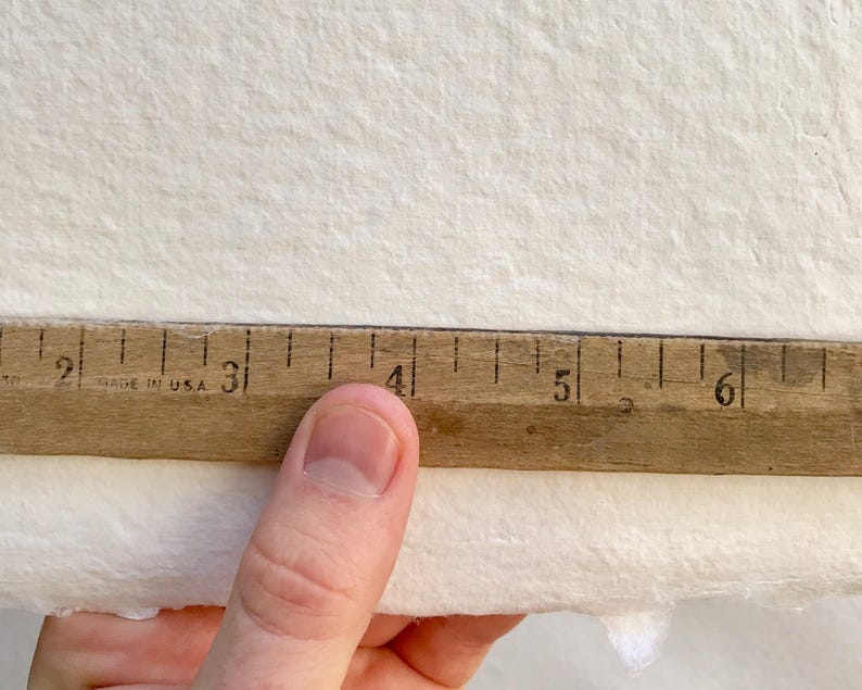 May include: A close-up of a wooden ruler with black markings, showing measurements from 1 to 6 inches. The ruler is resting on a white textured surface.