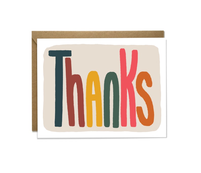 May include: A greeting card with the word "Thanks" in colorful, bold letters. The letters are in shades of blue, red, yellow, green, and orange against a beige background. The card is paired with a brown envelope.