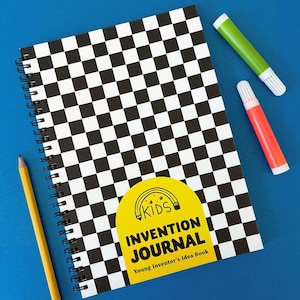 Könnte beinhalten: Ein spiralgebundenes Notizbuch mit einem schwarz-weiß karierten Muster auf dem Einband. Der Einband hat einen gelben Aufkleber mit dem Text "KIDS INVENTION JOURNAL" und "Young Inventor's Idea Book". Ein gelber Bleistift und zwei Filzstifte, einer grün und einer orange, sind ebenfalls zu sehen.