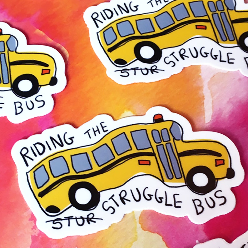May include: A yellow school bus sticker with the text "Riding the Struggle Bus" in black. The bus is tilted on its side, with the wheels facing upwards. The sticker is on a pink and orange watercolor background.