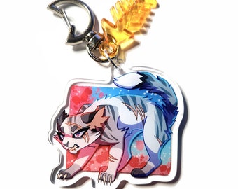 May include: A white and blue cat with orange and gray markings on a pink and blue background with white polka dots. The cat is looking to the left with a fierce expression. The image is printed on a clear acrylic keychain with a silver metal ring and a yellow plastic fish bone charm.