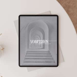 May include: A black tablet showing a grayscale image of an arched hallway with steps. The text "yourgates" is displayed, with more text below. The tablet is on a light grey surface, with a white table and a beige surface in the background.