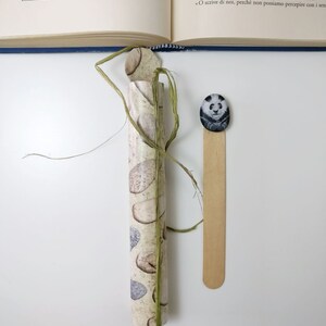 May include: A close-up of a rolled up piece of paper with a birch bark pattern. The paper is tied with a green string. A wooden bookmark with a panda bear illustration is to the right of the paper.