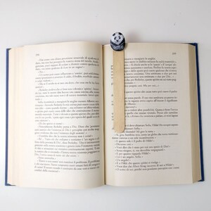 May include: A close-up of an open book with a wooden bookmark featuring a panda design. The book is open to a page with text in Italian. The bookmark is placed between the pages.
