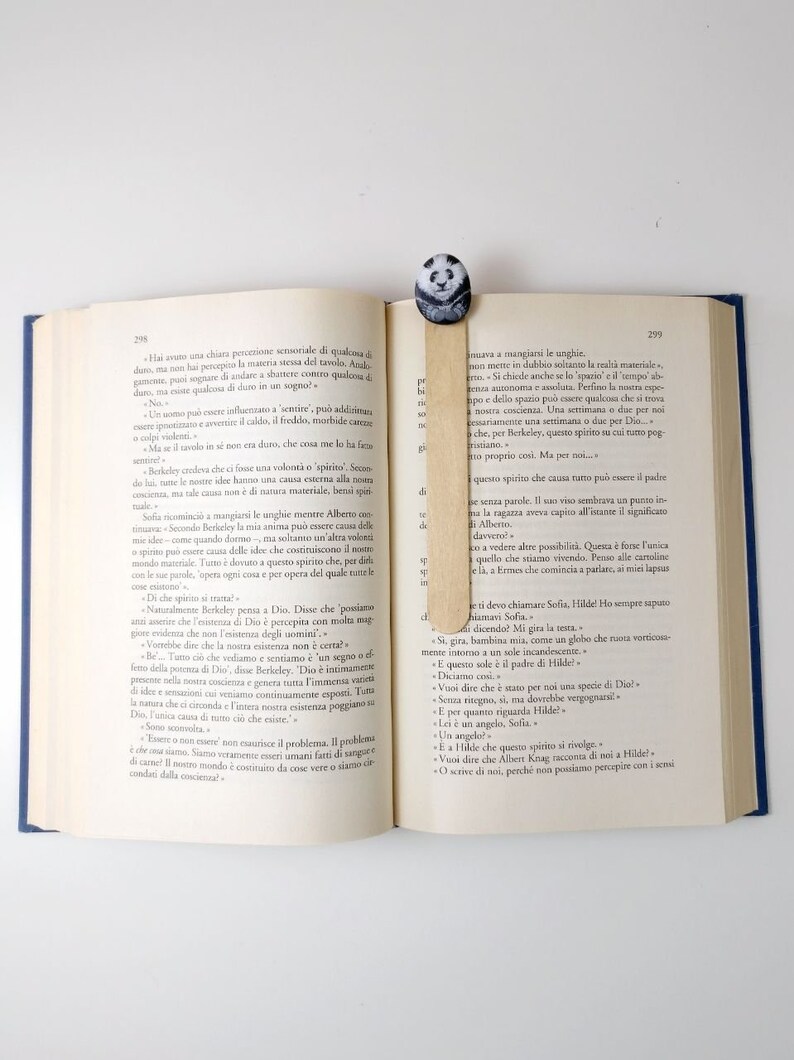 May include: A close-up of an open book with a wooden bookmark featuring a panda design. The book is open to a page with text in Italian. The bookmark is placed between the pages.