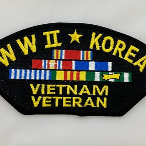May include: A black embroidered patch with yellow lettering that reads "WW II * KOREA VIETNAM VETERAN". The patch features a stack of colorful ribbons.