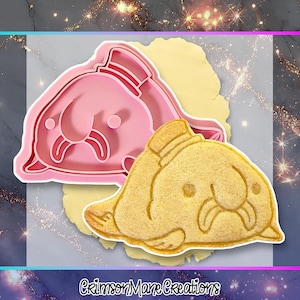 Könnte beinhalten: Ein rosa Kunststoff-Ausstecher in Form eines Blobfischs, neben einem gebackenen Blobfisch-Keks. Der Ausstecher hat ein detailliertes Design, und der Keks ist goldbraun. Das Bild enthält den Text "Crimson Mane Creations".