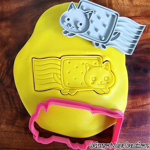May include: A yellow playdough base with a Nyan Cat cookie cutter imprint and two additional cookie cutters. One gray cookie cutter is a Nyan Cat, and the other is a pink outline of the Nyan Cat shape. The image includes the text "Crimson Mane Creations".
