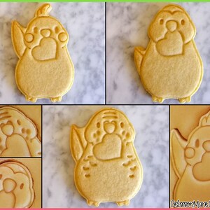 May include: Four sugar cookies decorated with a bird design. The cookies are light brown and have a heart shape on the chest of the bird. The cookies are on a white marble surface.