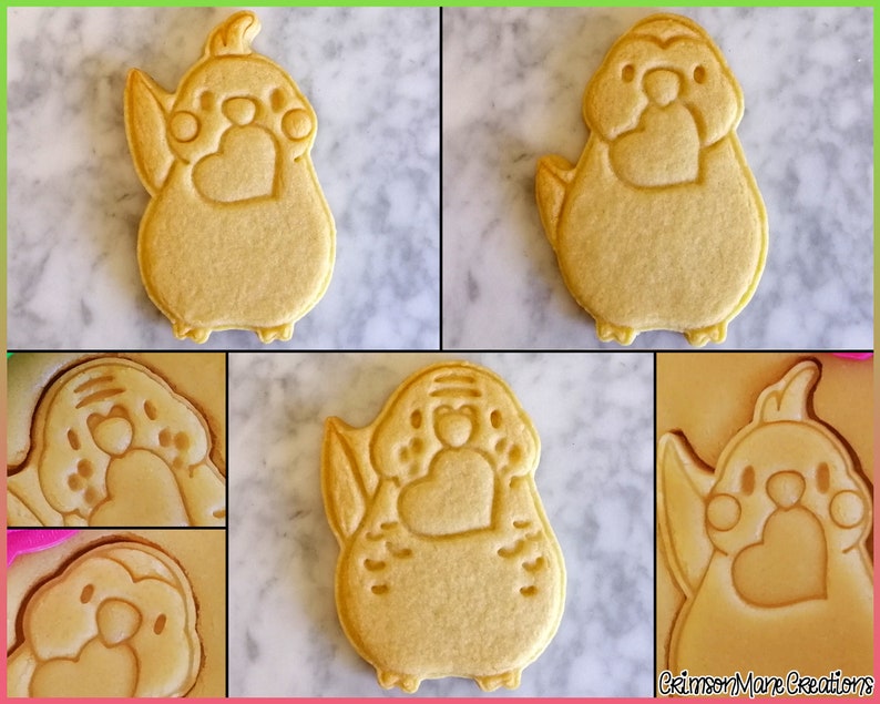May include: Four sugar cookies decorated with a bird design. The cookies are light brown and have a heart shape on the chest of the bird. The cookies are on a white marble surface.
