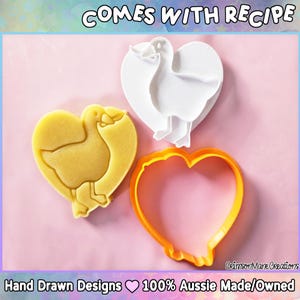May include: A heart-shaped cookie cutter set with a duck design. The set includes a yellow cookie, a white cutter, and an orange outline cutter. The text "COMES WITH RECIPE" is at the top. The bottom text reads "Hand Drawn Designs 100% Aussie Made/Owned."