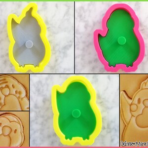 May include: Four cookie cutters in the shape of a bird. Two are yellow with a green bird inside, and two are pink with a gray bird inside. The cutters are shown next to cookies that have been cut with the cutters.
