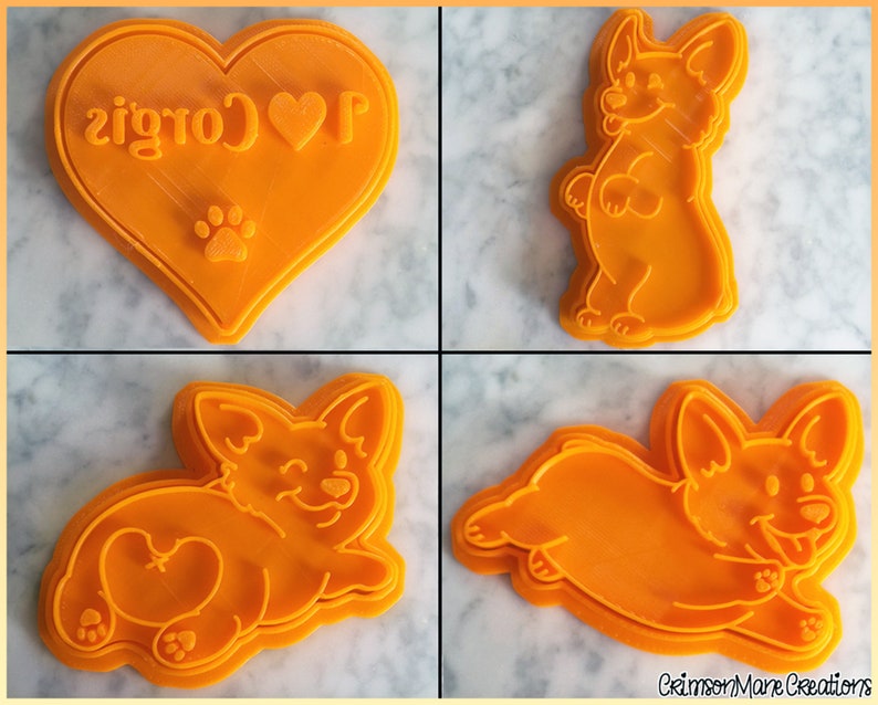 May include: A set of four orange plastic cookie cutters featuring a heart shape with the text I love Corgis and a paw print, a standing Corgi, a lying Corgi showing its rear, and a running Corgi. The text CrimsonMare Creations is visible.