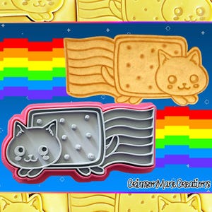 May include: Cookie cutters in the shape of a cat riding a rectangular cookie. The cat is light brown and the cookie is tan. A gray and pink cookie cutter is also shown. The background is blue with a rainbow.