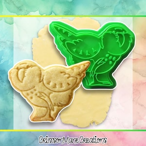 May include: A green plastic cookie cutter in the shape of a bird sits next to a bird-shaped cookie. The cookie is light brown and has detailed markings. The text "Crimson Mane Creations" is at the bottom.