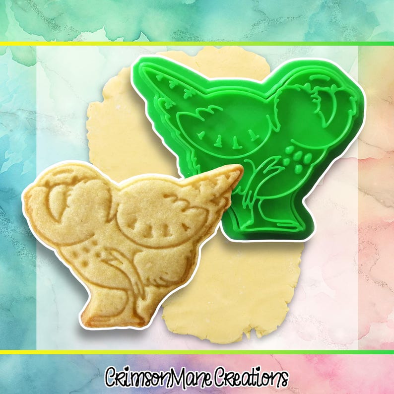 May include: A green plastic cookie cutter in the shape of a bird sits next to a bird-shaped cookie. The cookie is light brown and has detailed markings. The text "Crimson Mane Creations" is at the bottom.