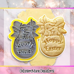 Peut inclure: Un emporte-pièce jaune et gris avec un motif de lapin et les mots "Happy Easter" dans une police décorative. À côté, un biscuit cuit avec le même motif. L'image a un fond rose et doré. Idéal pour Pâques.