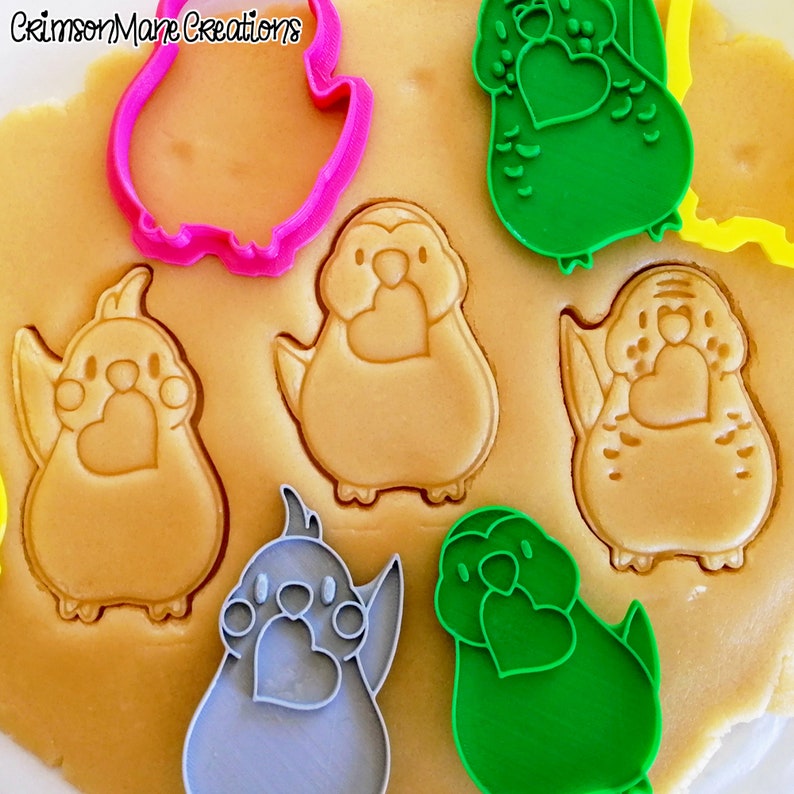 May include: A set of cookie cutters in various shapes and colors, including a bird, a heart, and a paw print. The cutters are made of plastic and are designed for use with cookie dough.