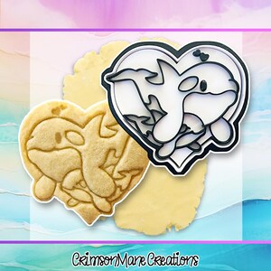 May include: A black heart-shaped cookie cutter featuring an orca whale design and a matching heart-shaped cookie with an embossed orca whale pattern. The text CrimsonMane Creations is printed at the bottom of the image in a black script font.
